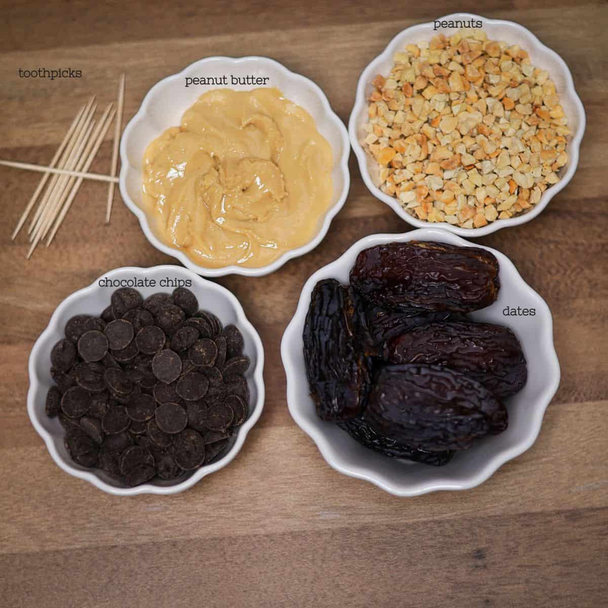 An overhead view of ingredients for chocolate covered stuffed dates: medjool dates, natural peanut butter, chocolate chips, crushed peanuts, and toothpicks.