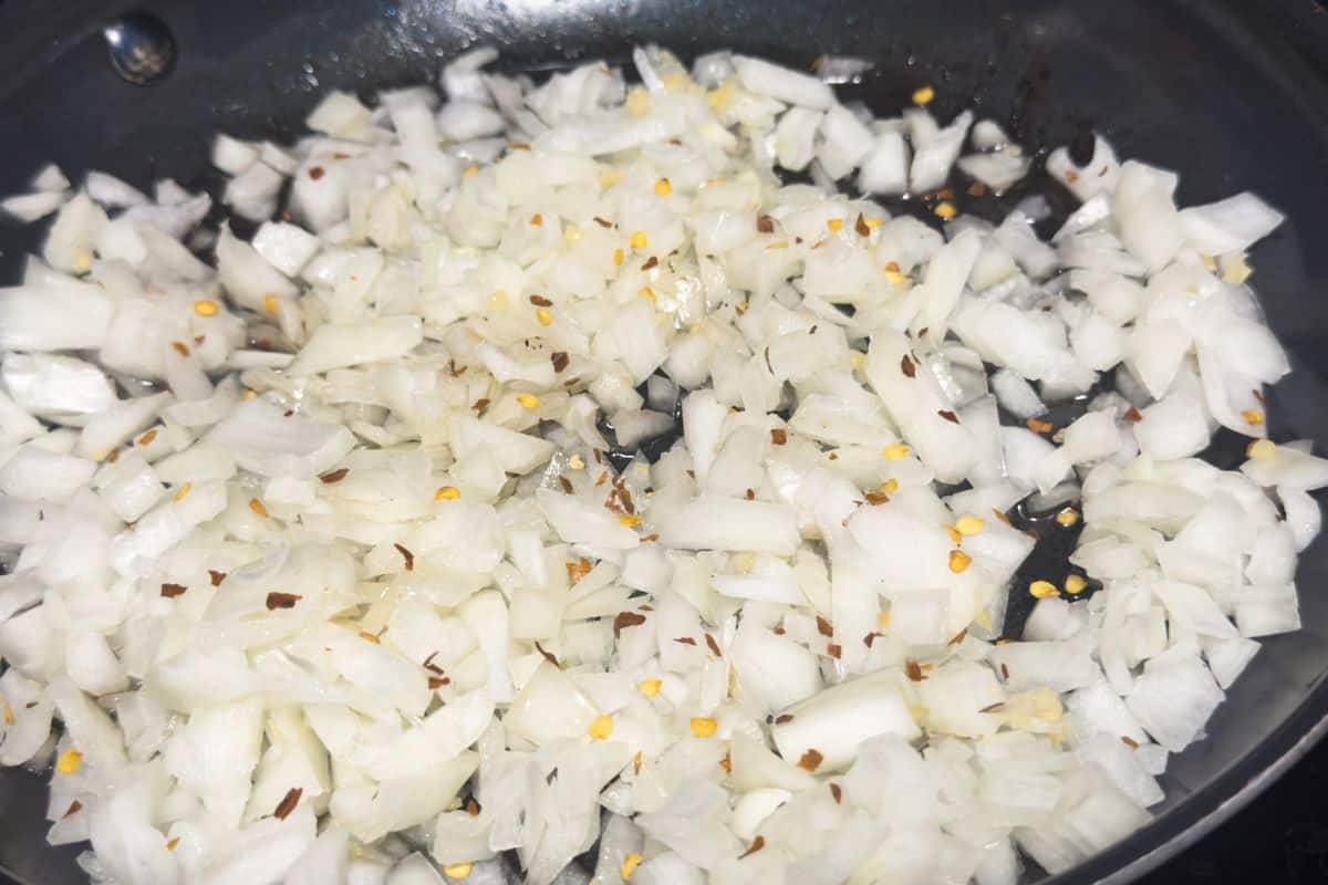 Onions and garlic sautéing in a skillet with red pepper flakes for keto casserole preparation.