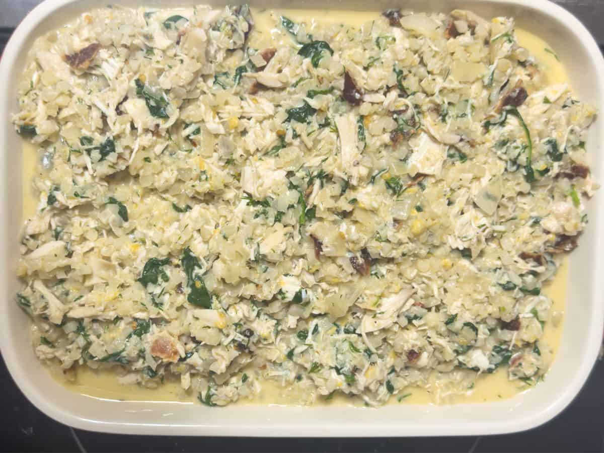 A baking dish filled with mixed ingredients for keto chicken and cauliflower rice casserole before baking.
