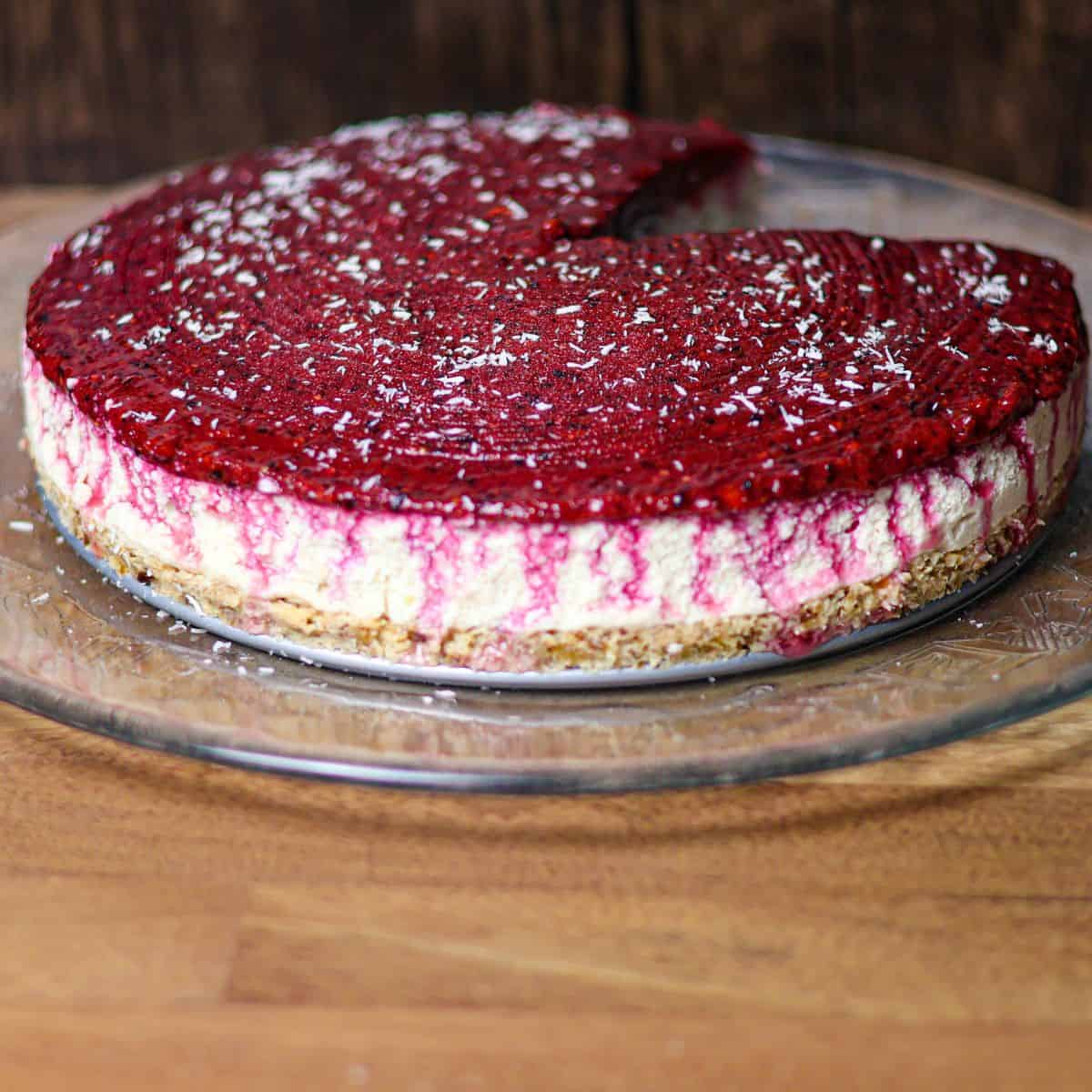 A fully garnished no-bake berry cheesecake with a rich red topping and sprinkled coconut on a glass serving dish.