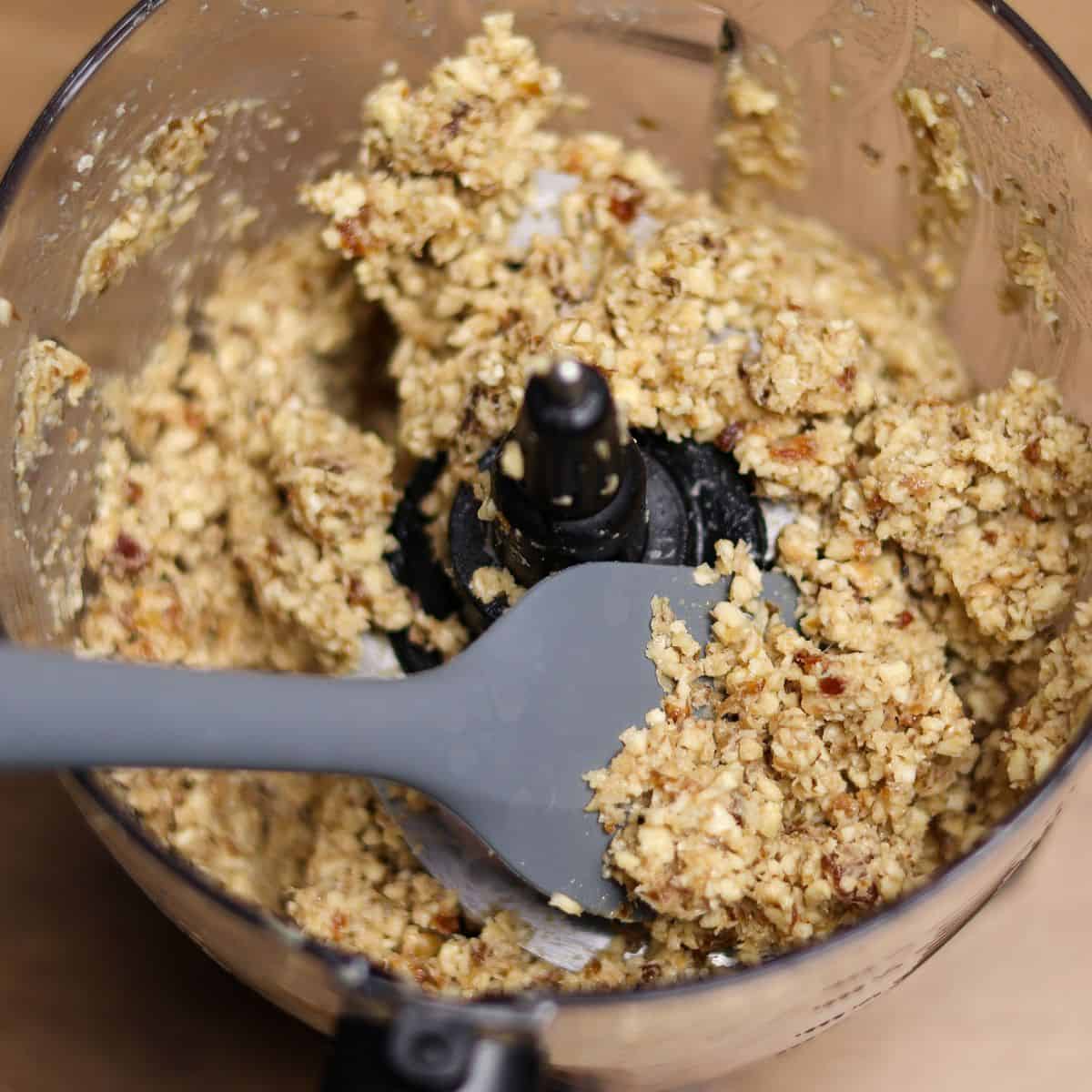 A food processor with mixed walnuts and dates for a no-bake berry cheesecake crust, showing a crumbly texture.