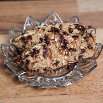 A close-up of a sliced piece of sprouted oat banana bread with visible chocolate chips, placed on an elegant glass serving plate.
