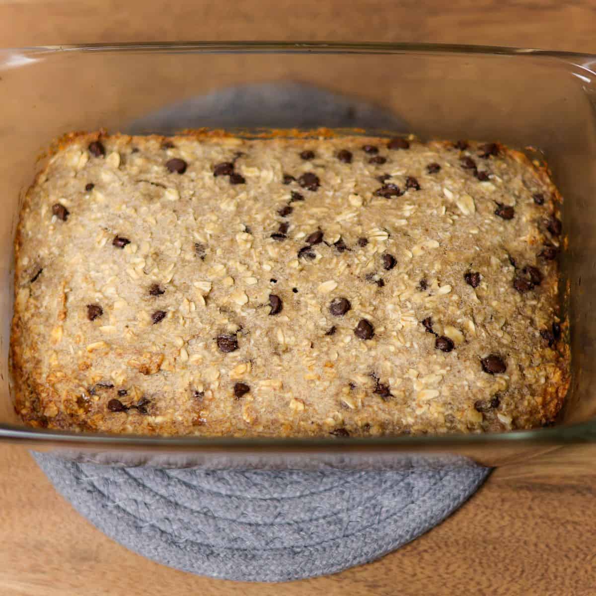 Sprouted oat banana bread with visible chocolate chips in a glass loaf pan just baked sitting on a grey hot pad.