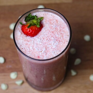 A vibrant pink Bahama Mama smoothie in a glass, topped with a strawberry and sprinkled with coconut, ready to be enjoyed.