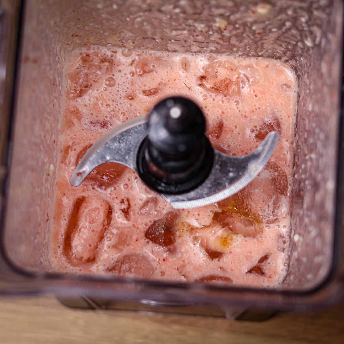 Top-down image of a blender showing a blended pink smoothie with ice cubes on top, ready for the final blend.