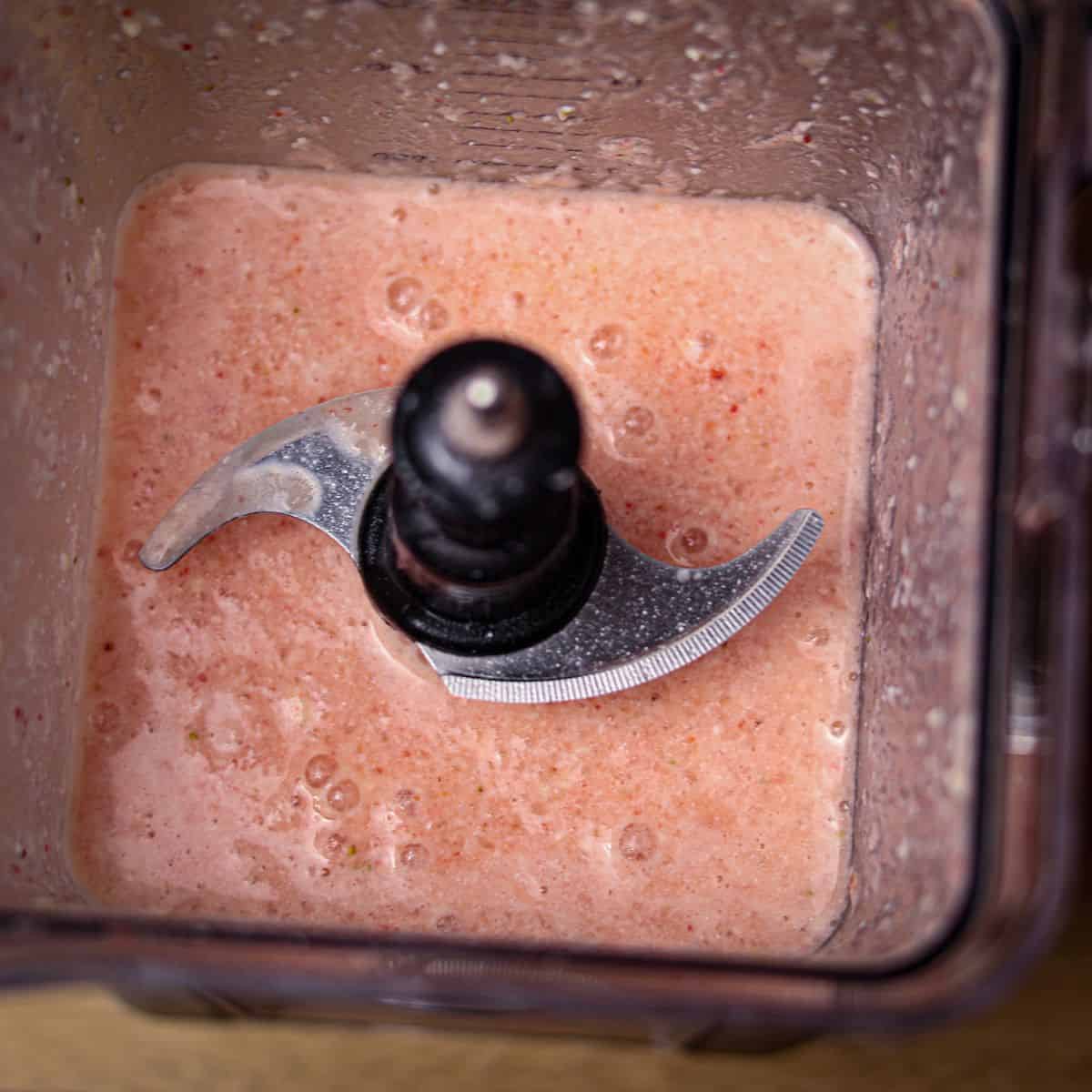 Close-up of a creamy, frothy pink smoothie in a blender, showing a blended mixture ready to be served.