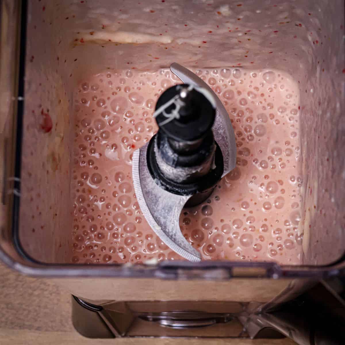 A creamy pink strawberry banana smoothie blend inside a blender, with bubbles on the surface indicating a freshly blended texture.