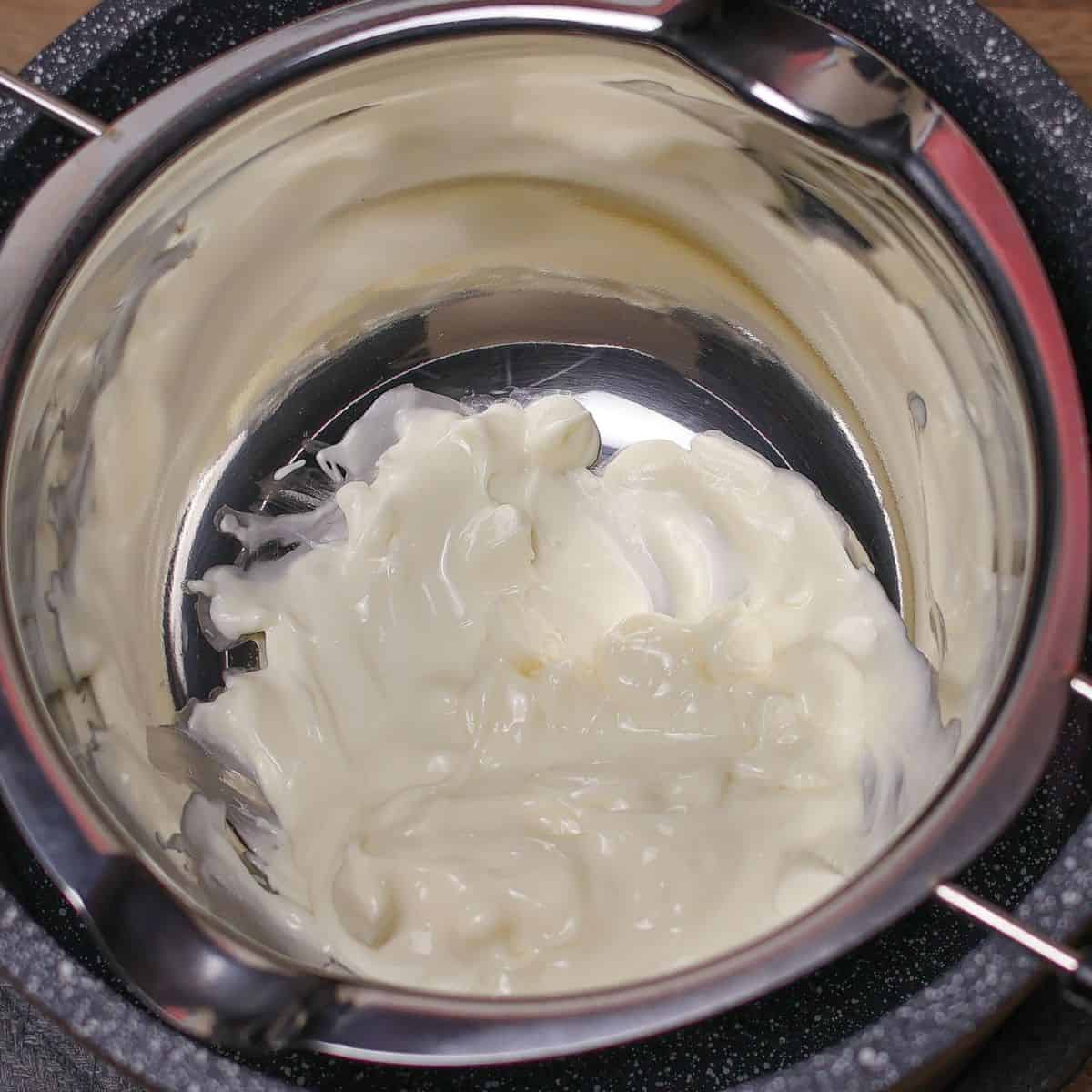 Melted white chocolate in a stainless steel bowl set over a pot of simmering water, illustrating the double boiler method for melting chocolate.