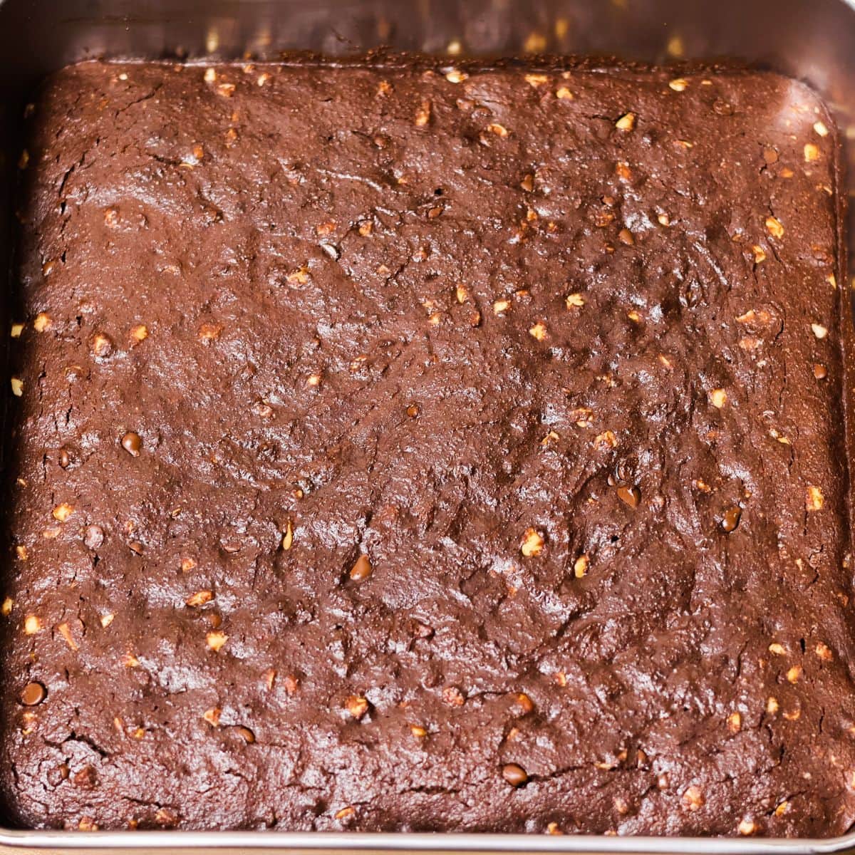 A full square baking dish of uncut dairy-free gluten-free brownies with visible nuts and chocolate chips baked into the top.