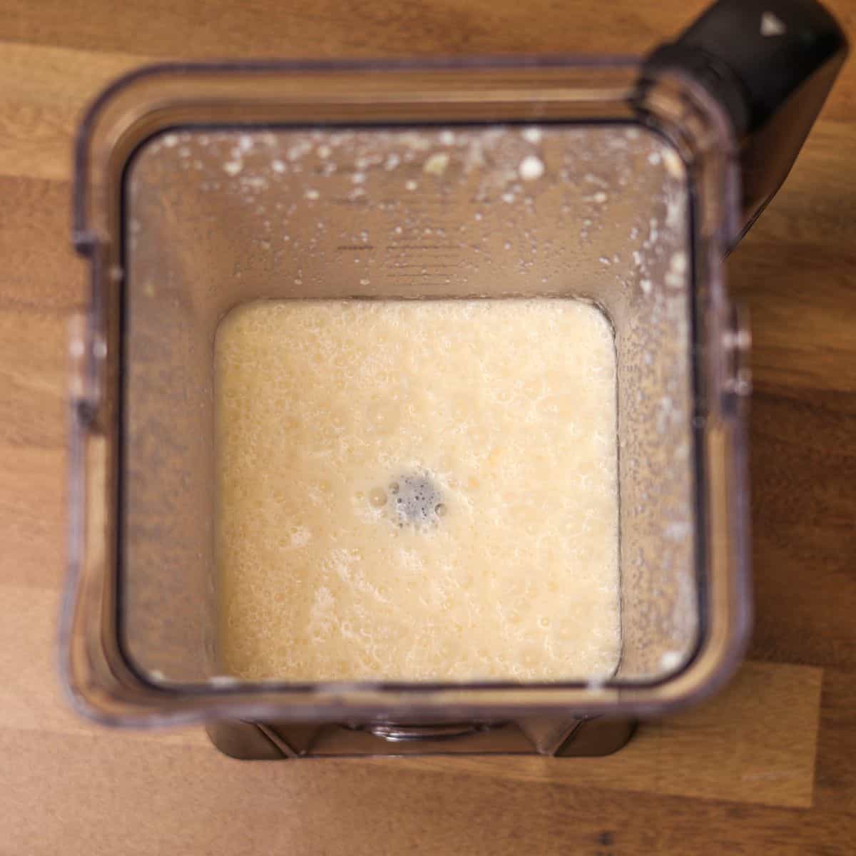 Top view of a blender filled with a frothy, pale yellow mixture of egg whites and other ingredients, ready to be poured.