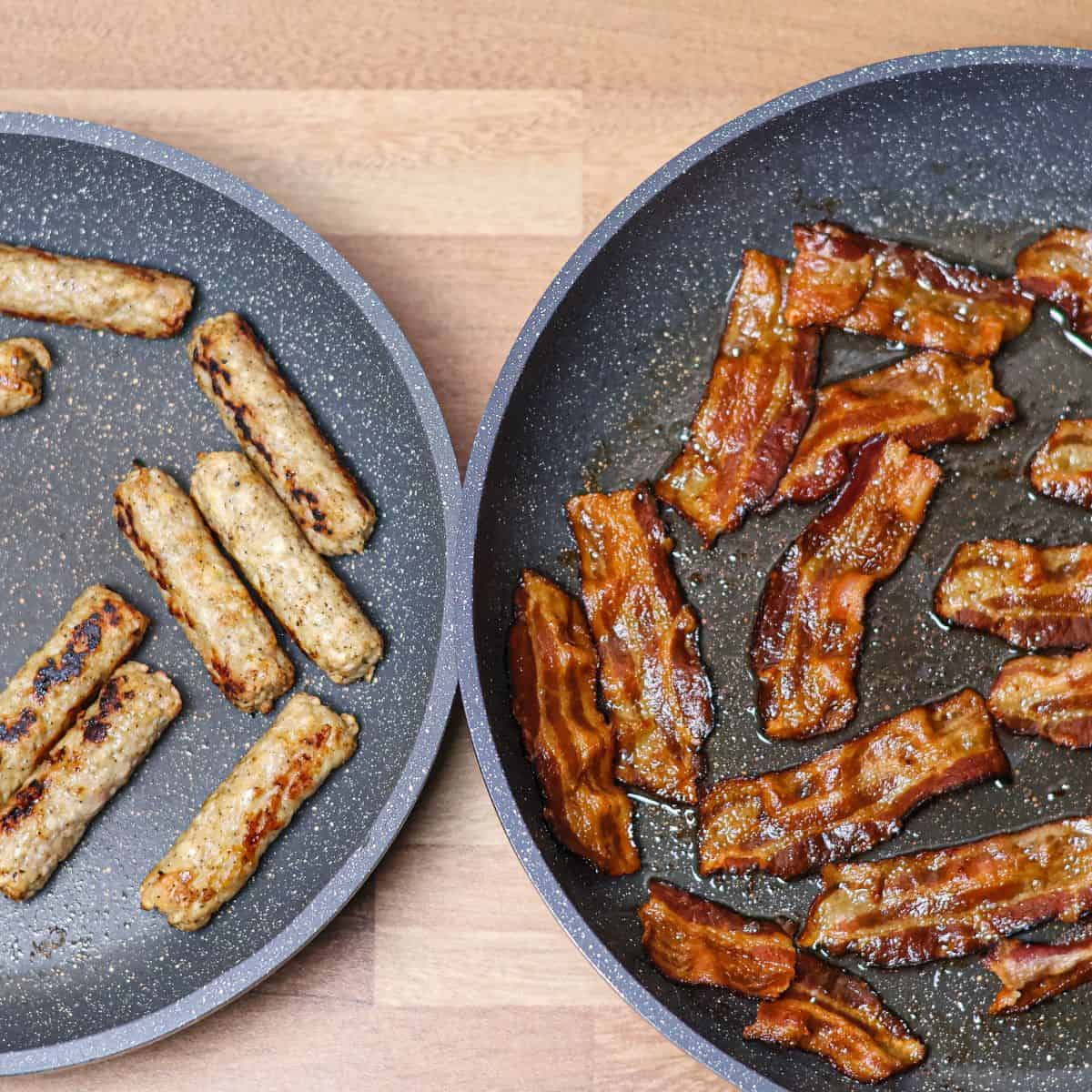 A non-stick skillet with turkey sausage links and bacon strips being cooked, showing the sausage browned and bacon crispy.