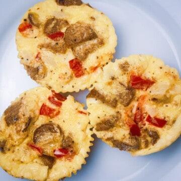 Close-up of savory keto egg bites on a cooling rack, highlighting the melted cheese and chunks of turkey sausage and red bell pepper.