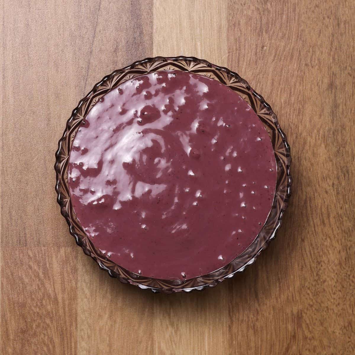 Overhead view of a glass bowl on a wooden surface filled with a smooth, purple acai blend, ready for toppings.