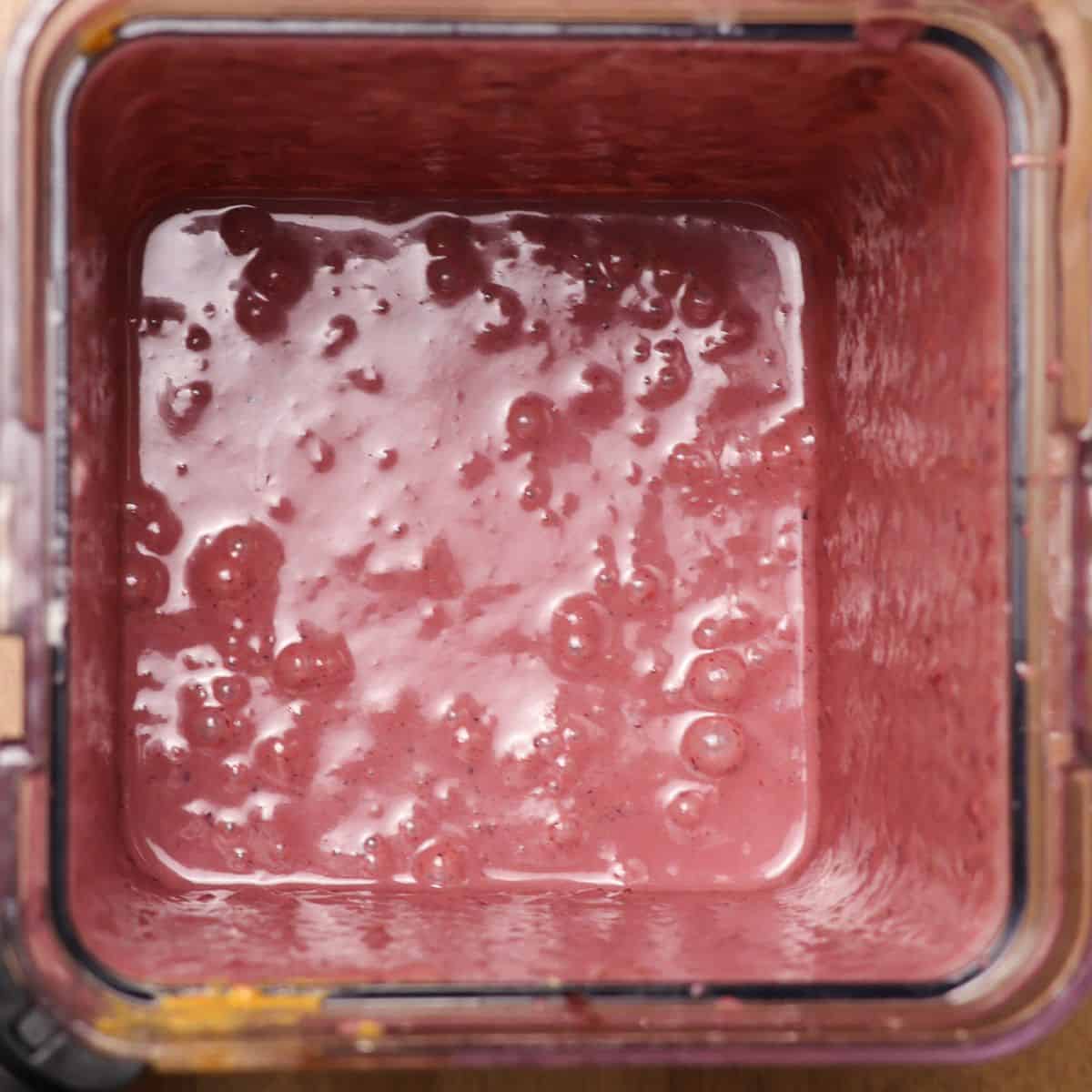 Top view of a blender containing a freshly blended acai mixture, showing a creamy purple texture with air bubbles on the surface.