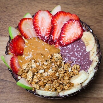 Close-up of the finished acai peanut butter bowl with neat toppings of granola, peanut butter, and sliced fruits including bananas, strawberries, and green apple.