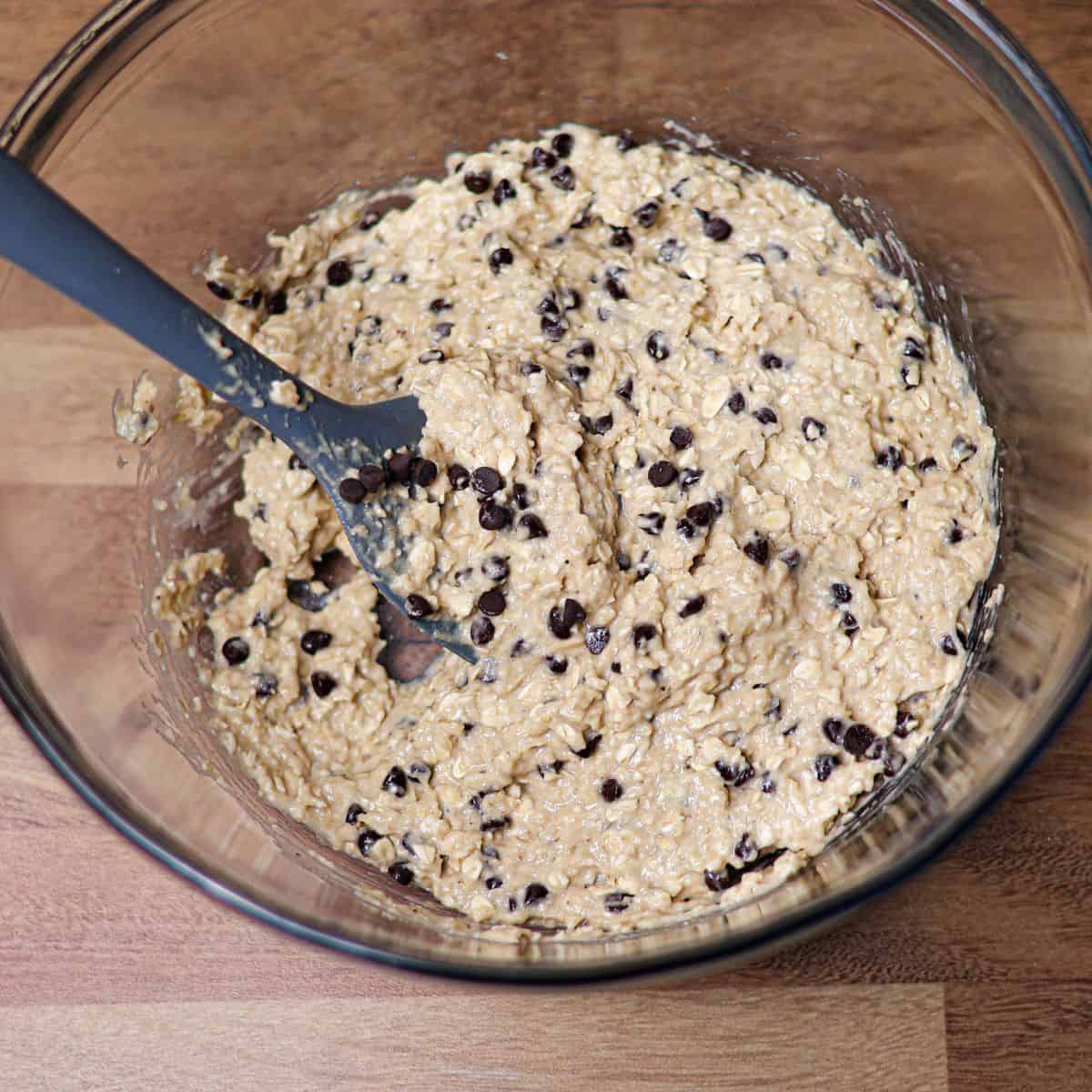 Large bowl with sprouted oat banana bread batter being folded with a spatula, mixing in dark chocolate chips