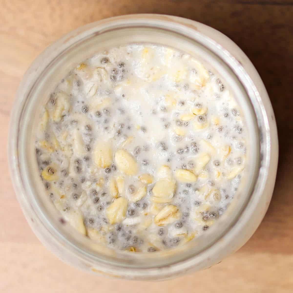 Overnight oats with coconut milk in a glass jar, soaked and ready after being refrigerated overnight, showing the thickened texture of the oats and chia mixture.