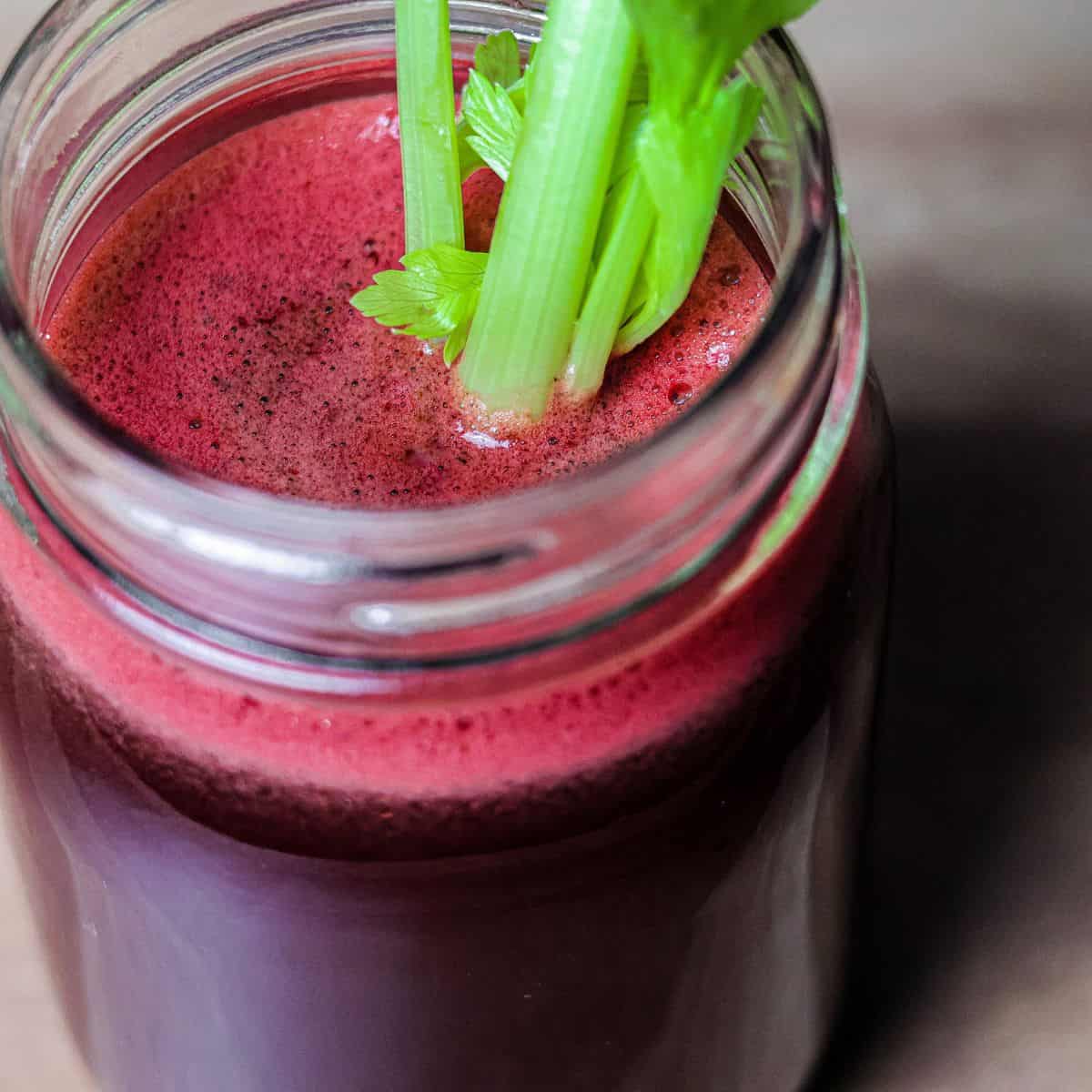 A close-up of a vibrant, red-hued juice in a mason jar garnished with a celery stick, indicating a nutrient-rich fresh juice.