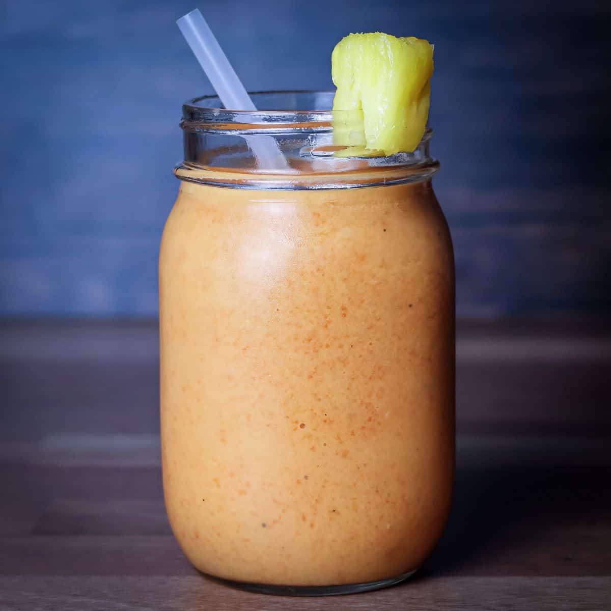A finished smoothie in a glass jar garnished with a pineapple wedge, resembling a recipe from Smoothie King.