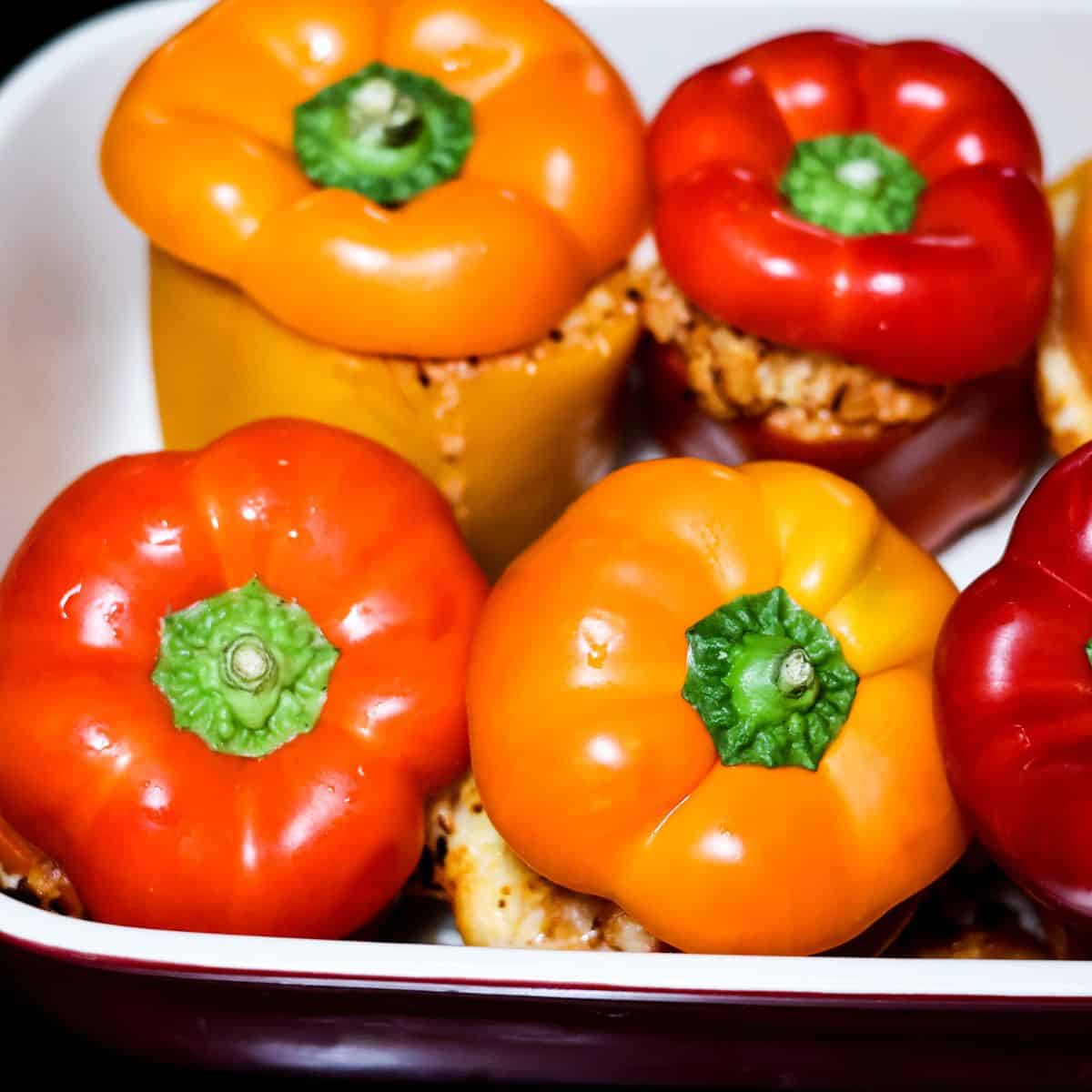 Colorful bell peppers filled with the meat and cheese mixture, placed in a casserole dish with their tops placed back on during the final minutes of baking.