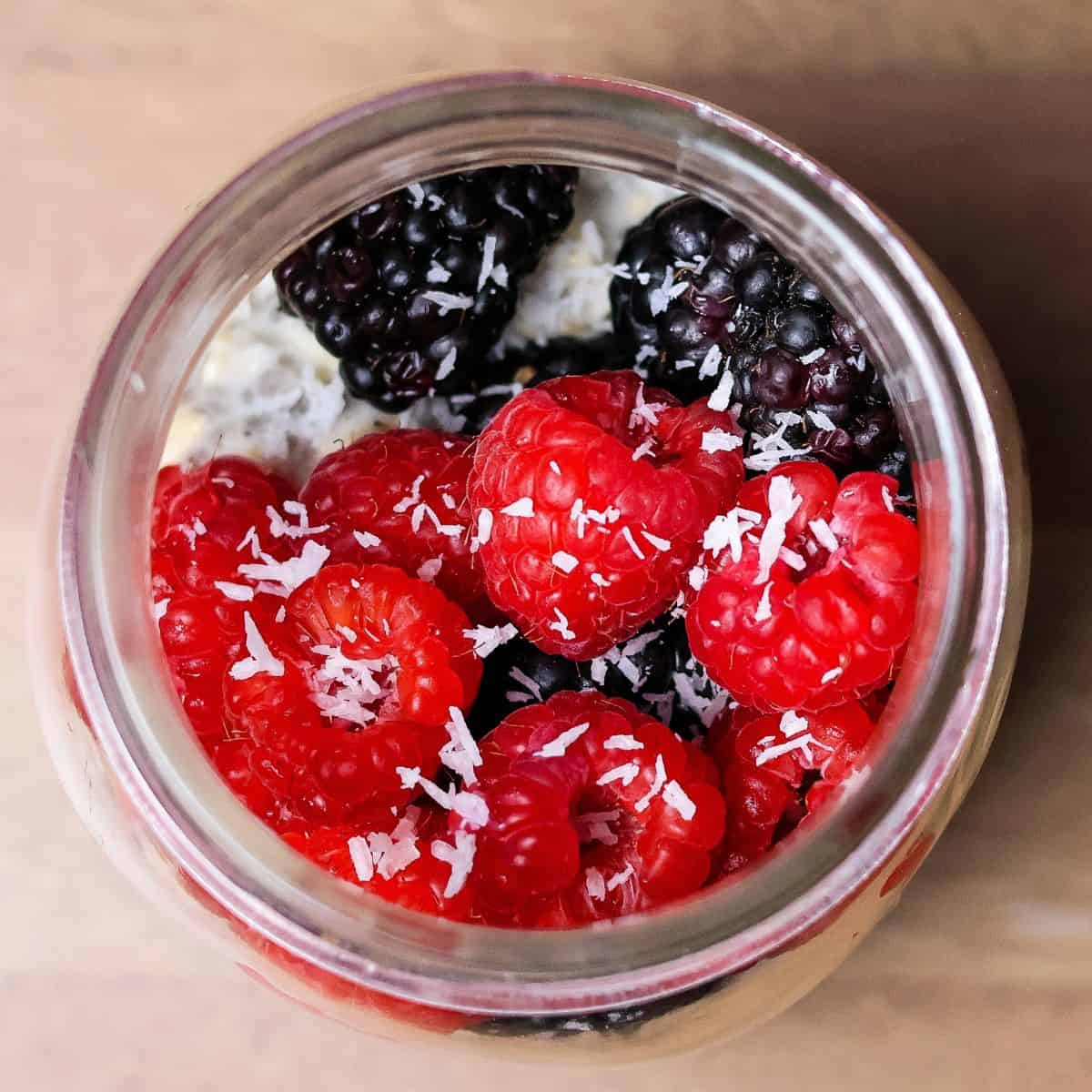 Top view of a mason jar with overnight oats, showcasing a vibrant layer of blackberries, raspberries, and a sprinkle of coconut shreds on top.