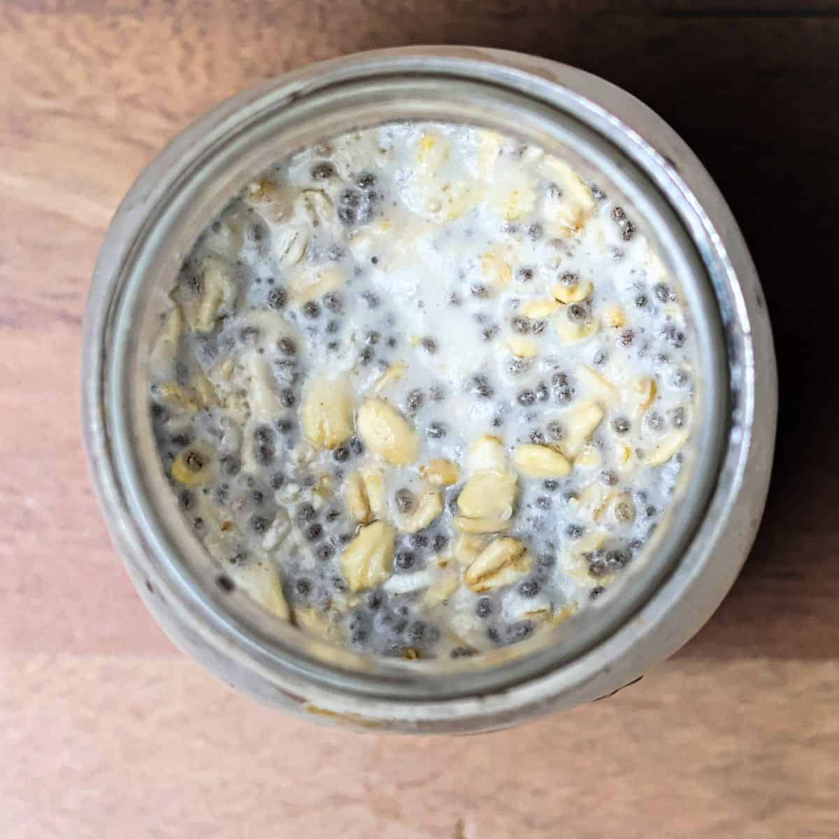 A glass jar with a mixed combination of overnight oats ingredients, including coconut milk, before the refrigeration process.