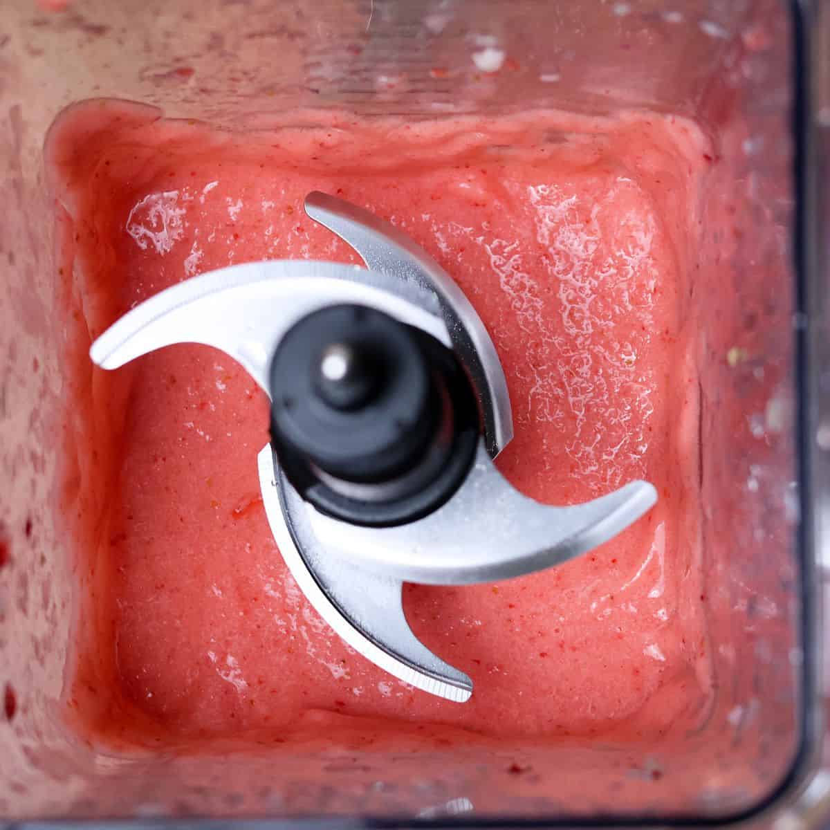 Top view of a blender with a freshly blended pink strawberry smoothie, the blades coated with the thick mixture.