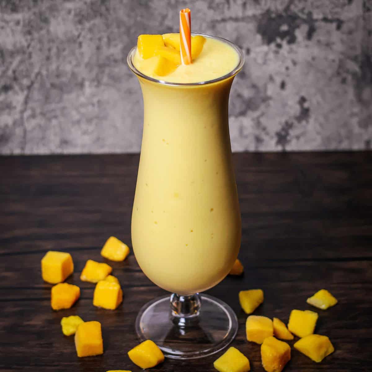 A finished mango a go go smoothie in a tall glass with an orange straw garnished with mango chunks i