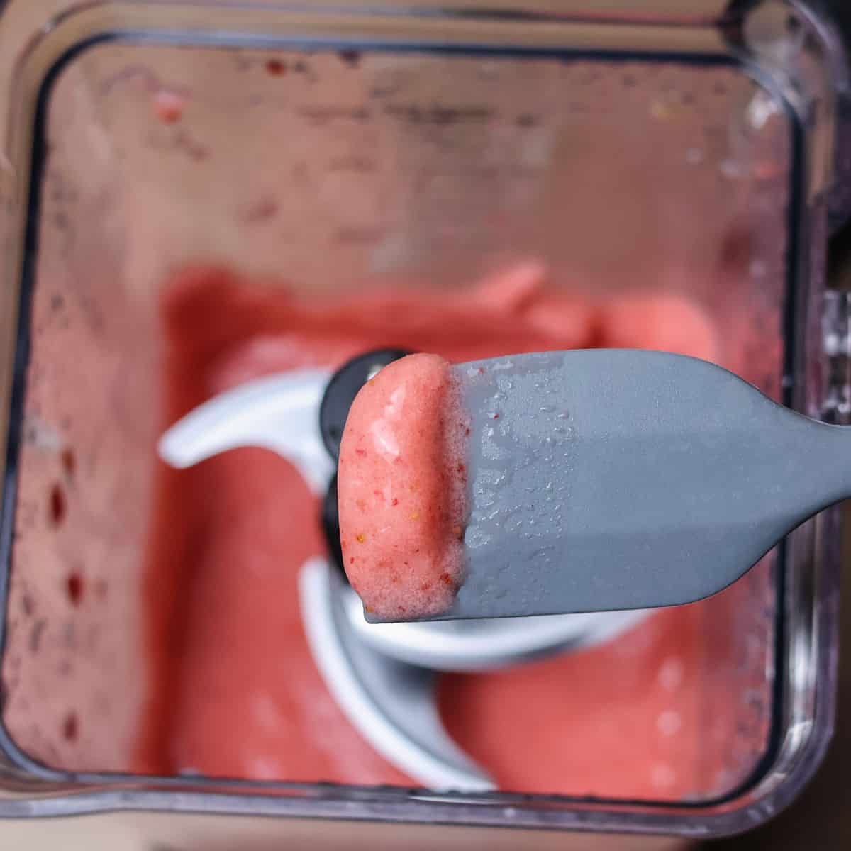 Close-up of a blender’s blade with a dollop of thick strawberry banana smoothie on a spatula, showing the creamy texture.