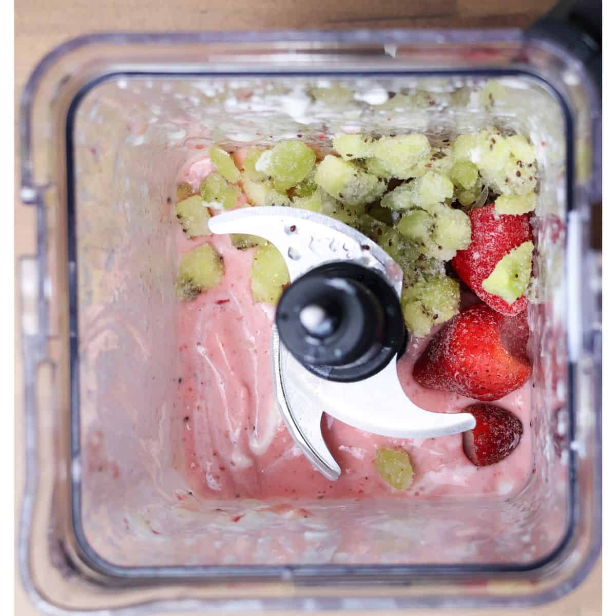 The blender now shows a half-blended mixture with more frozen kiwi and strawberries visible, suggesting ingredients have been added to adjust the consistency of the smoothie.