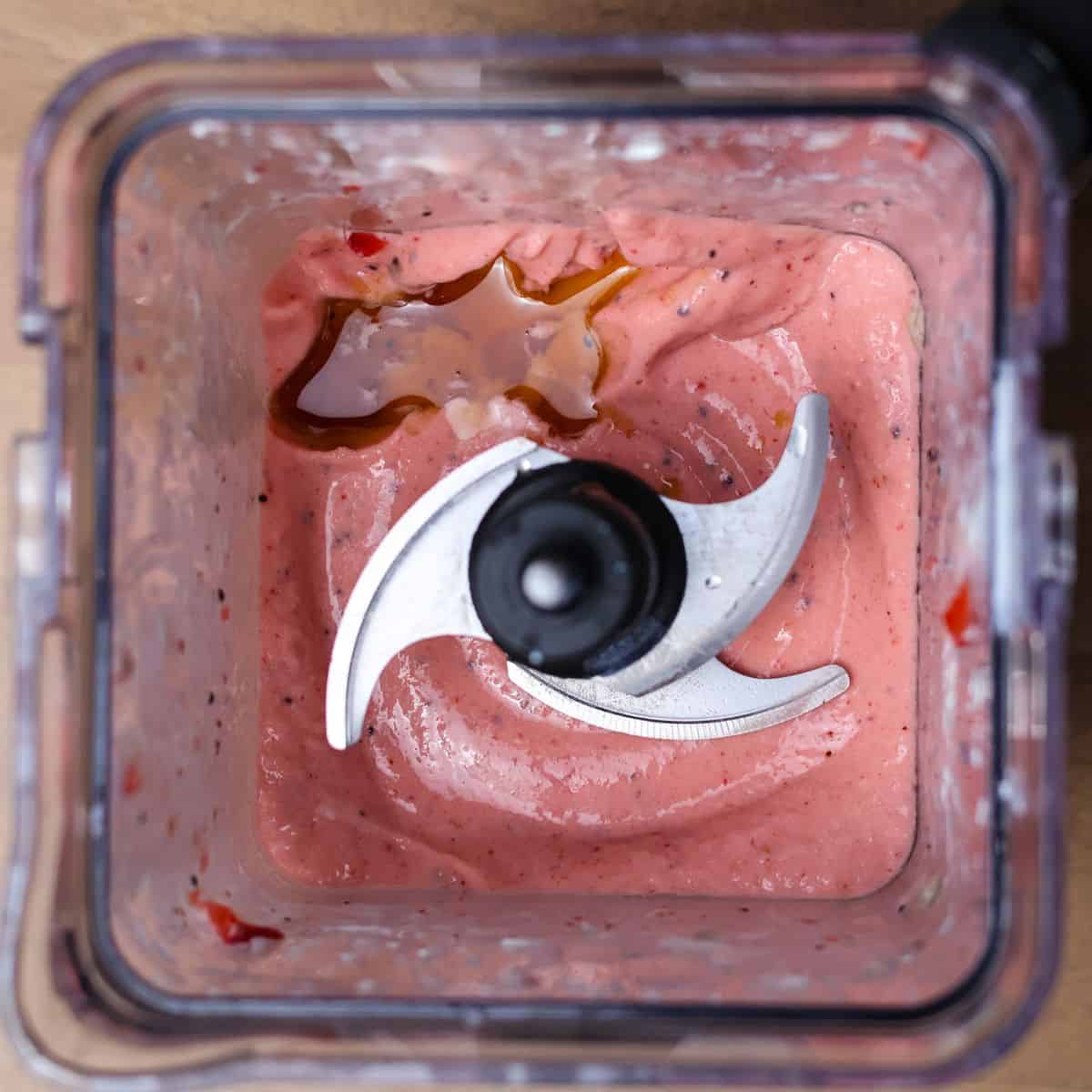 A closer view inside the blender shows the smoothie with a vibrant pink hue, and maple syrup has been drizzled on top, indicating flavor adjustment.