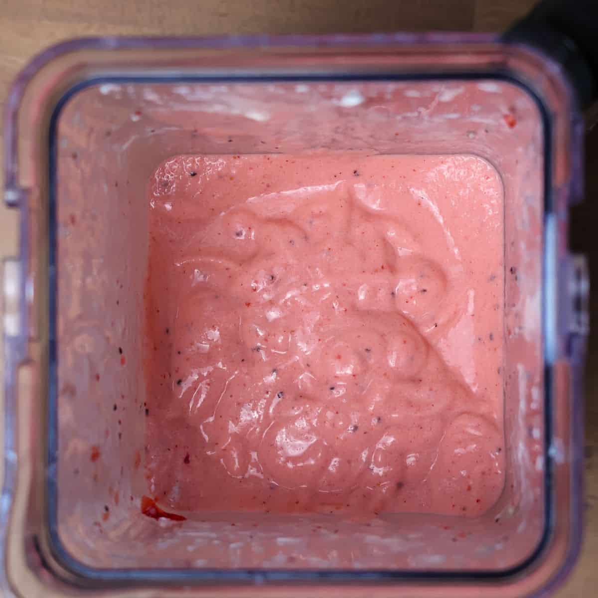 Top-down view of the final blended kiwi quencher in the blender, showing a smooth, creamy texture with specks of kiwi and strawberry seeds.