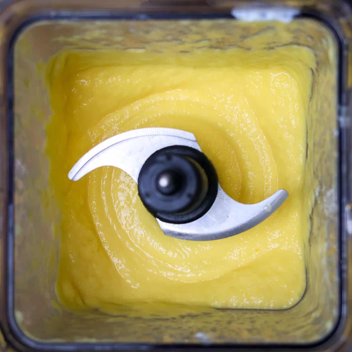 The final blend of a creamy mango smoothie view inside of a blender.