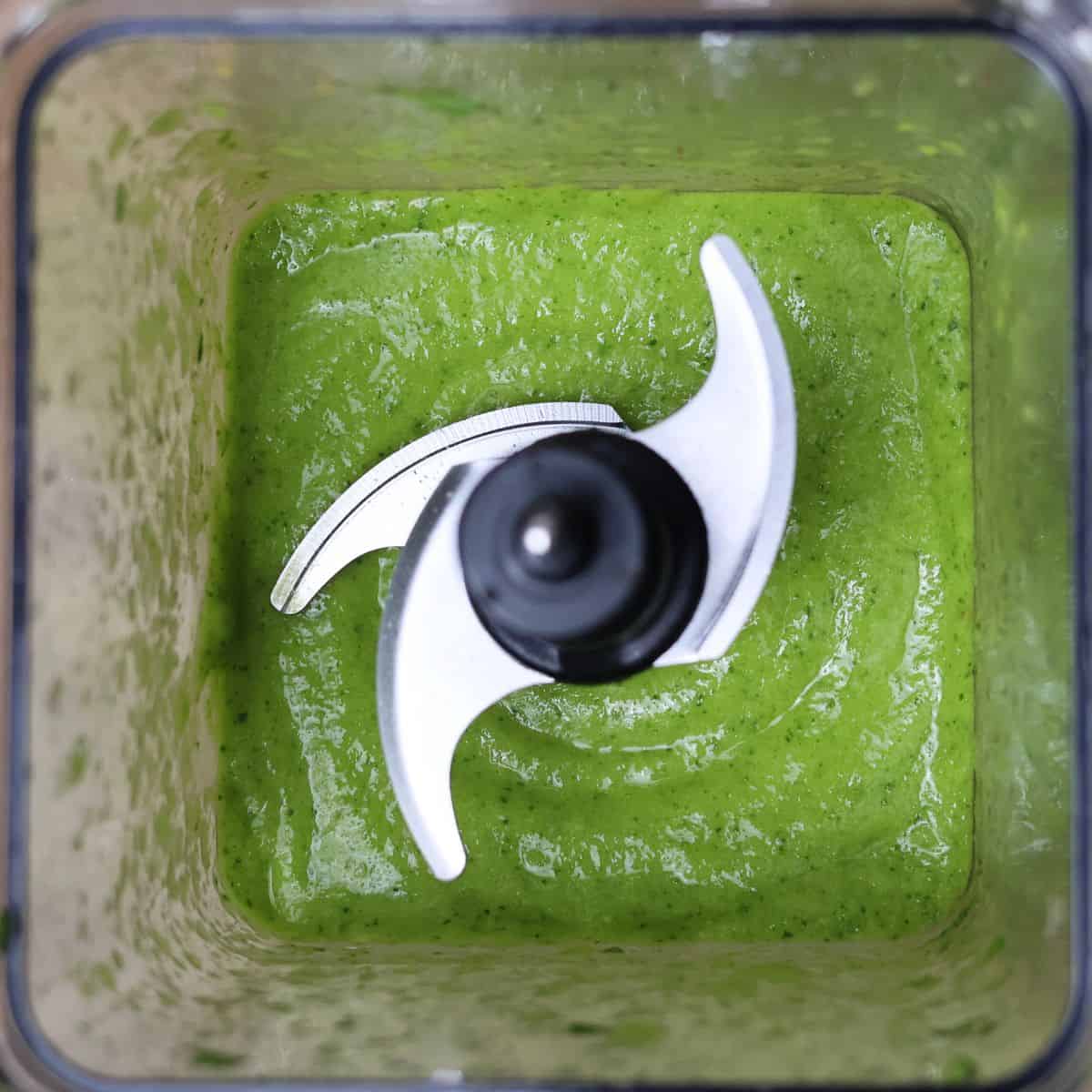 A top-down image capturing a thick, evenly blended green smoothie in a blender, with a smooth surface.