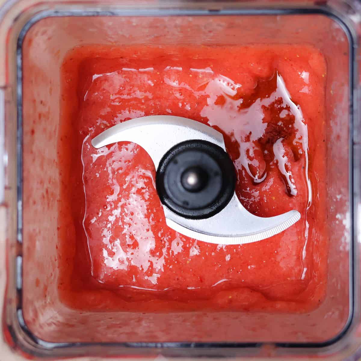 Top-down view inside a blender showing a bright red smoothie blend with added maple syrup, ready to blend again after adjusting flavors.