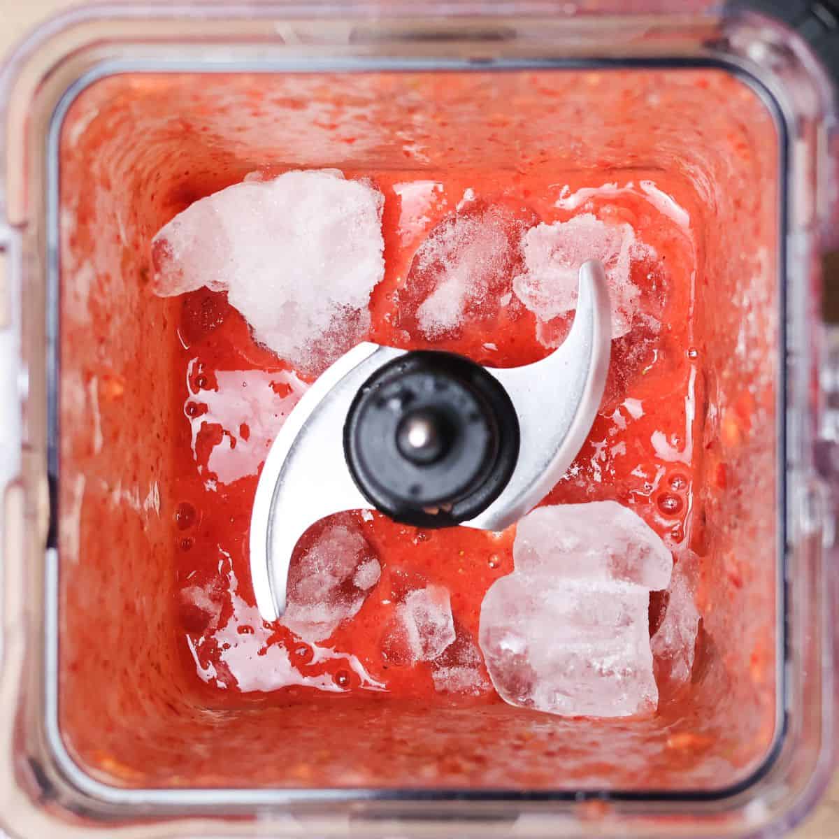 A blender view from above with a bright red smoothie mixture with added ice cubes to adjust the consistency.