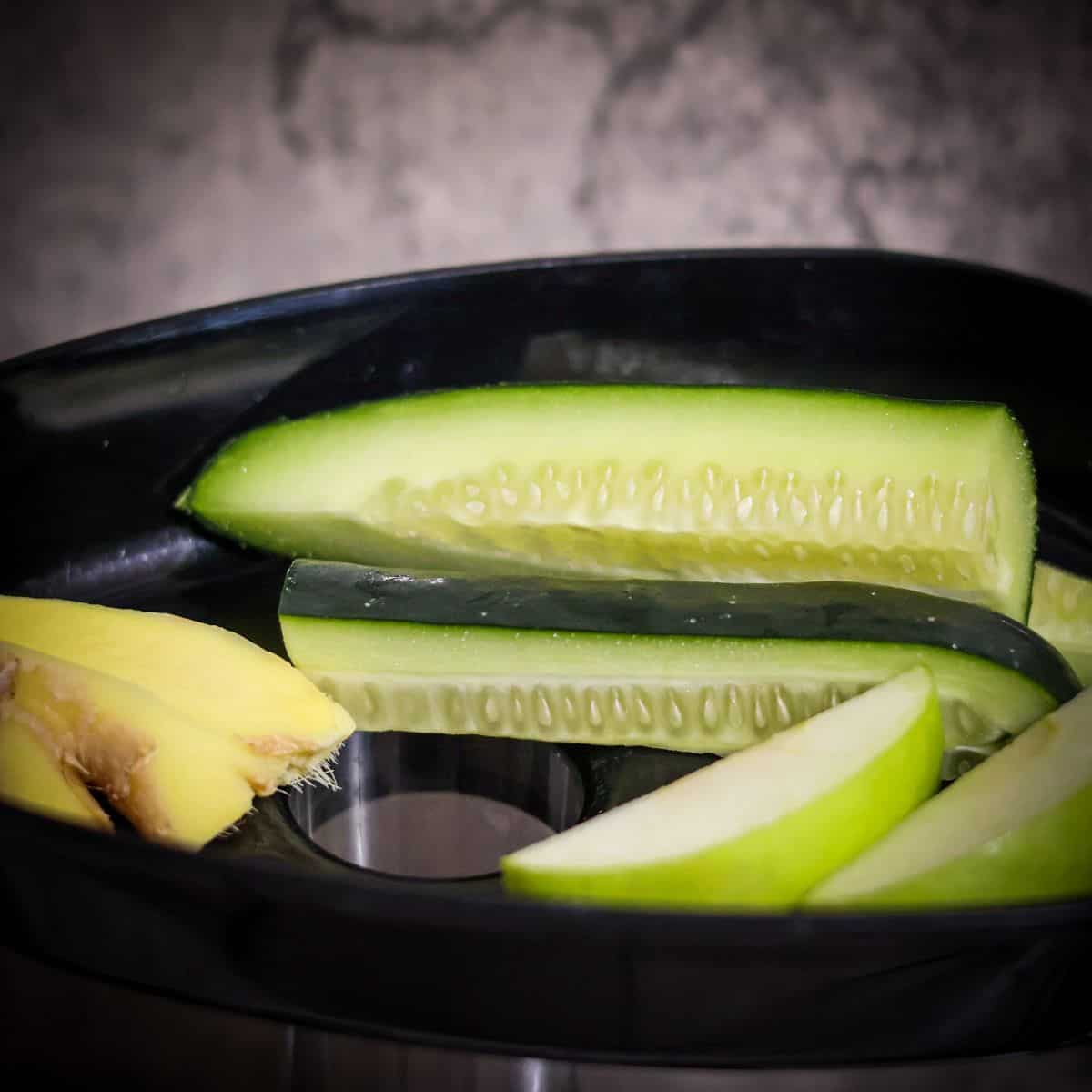 Slices of cucumber, green apple, and pieces of ginger in a juicer tray, ready for juicing.