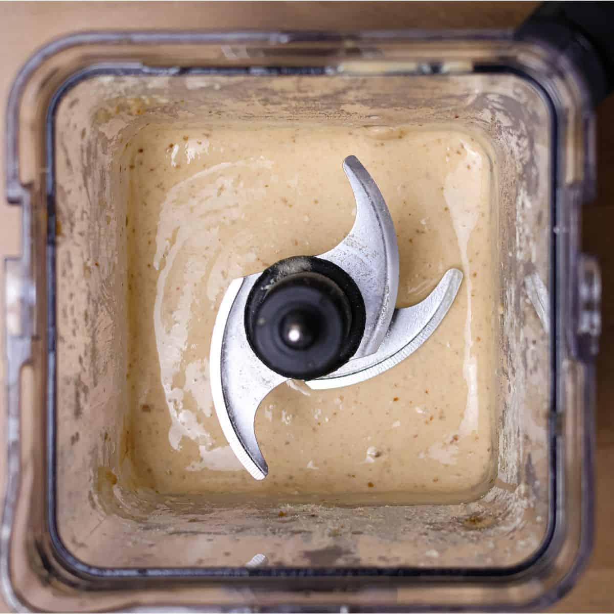Top view of a creamy, light beige smoothie in a blender, showing a smooth and thick texture after adjusting the consistency.