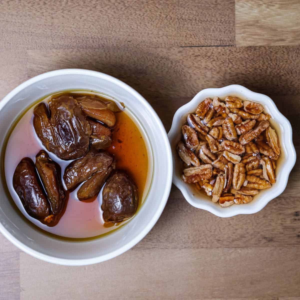Soaked and pitted dates in a bowl of water next to another bowl of soaked pecans, prepared for blending into a smoothie.