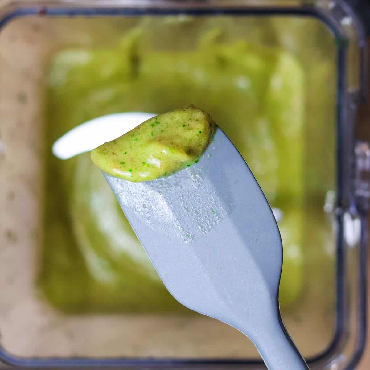 Close-up of a spatula with a spoonful of green smoothie mixture taken from a blender.