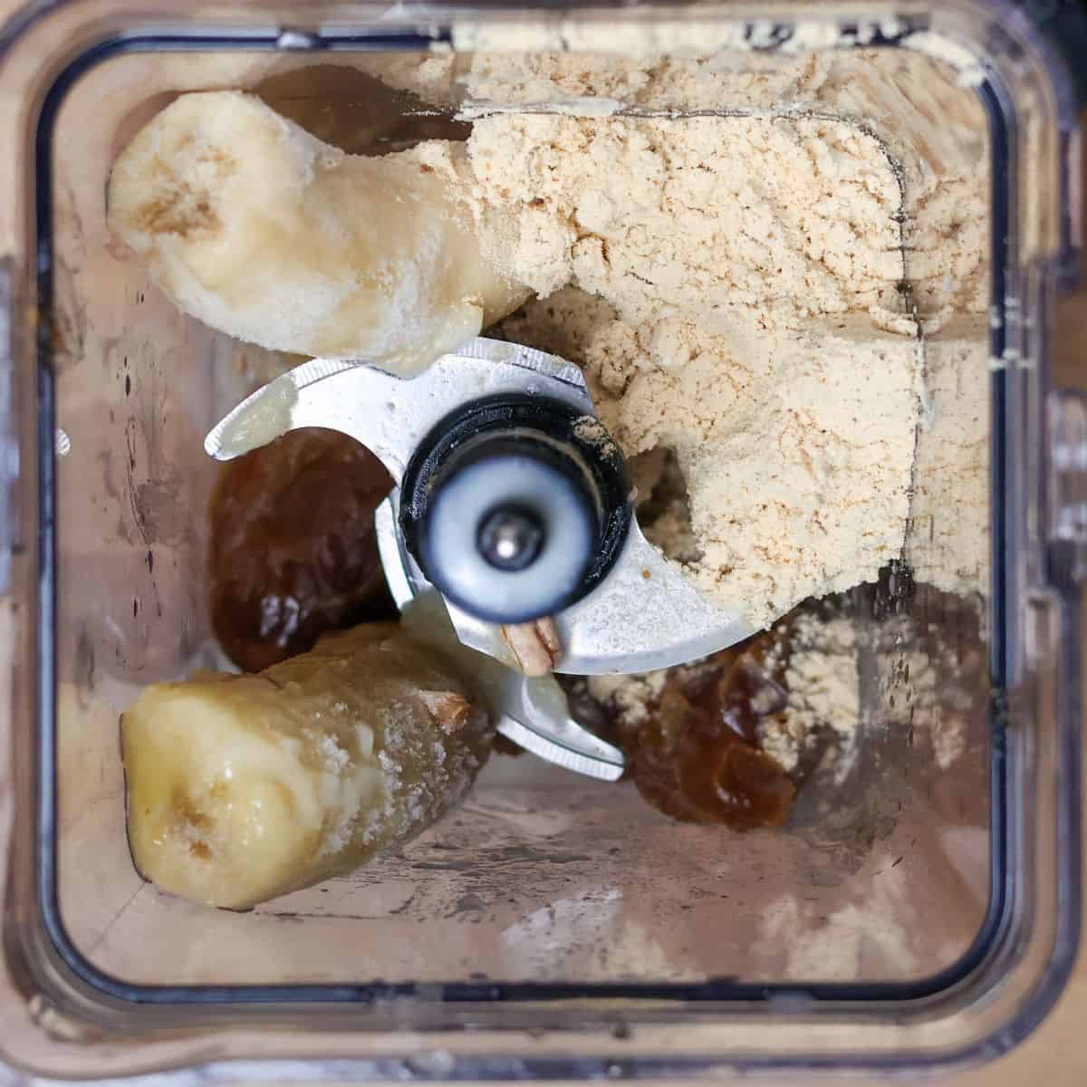 Top view of a blender filled with ingredients for a Hulk smoothie copycat recipe, including frozen bananas, pecans, vanilla protein powder, and dates before blending.
