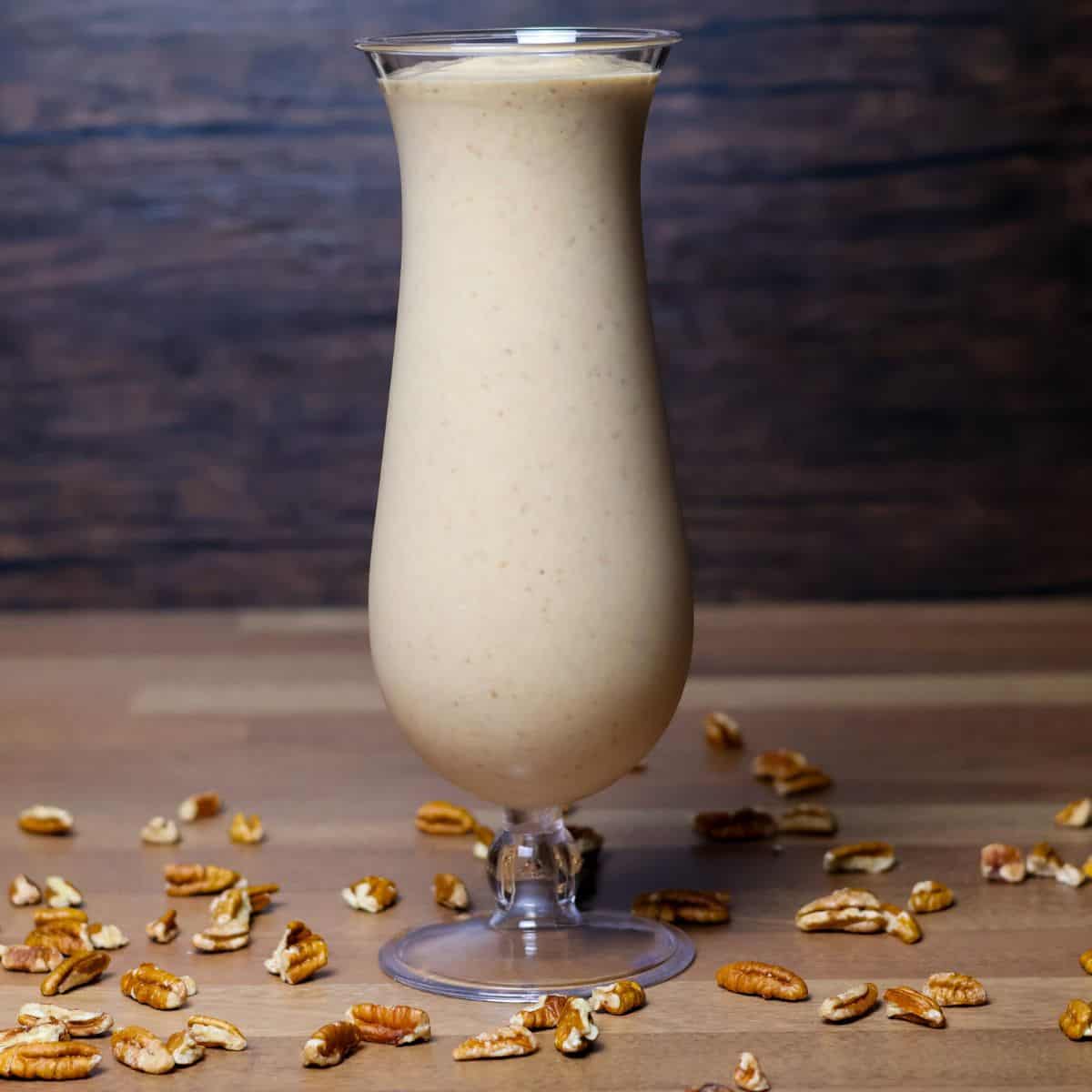 A tall glass of creamy Hulk smoothie served on a wooden table, with the surface sprinkled with crushed pecans for added texture and flavor.