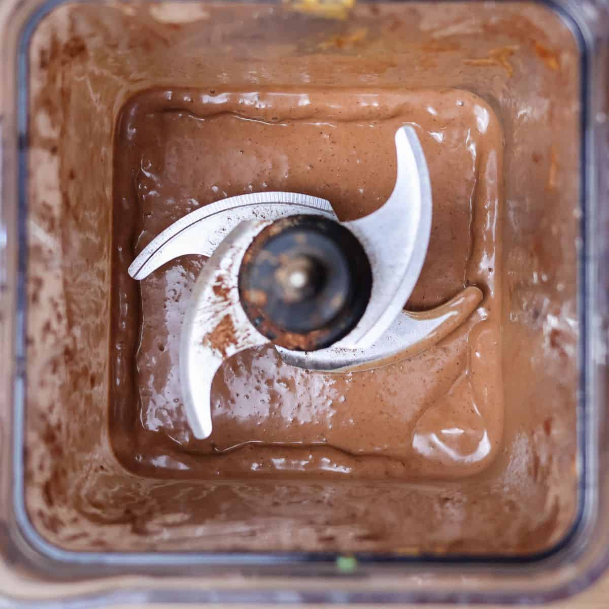 A blender jar filled with chocolate smoothie. The smoothie is a dark, rich brown color and has a smooth, viscous texture. There are no visible chunks of chocolate or other ingredients.