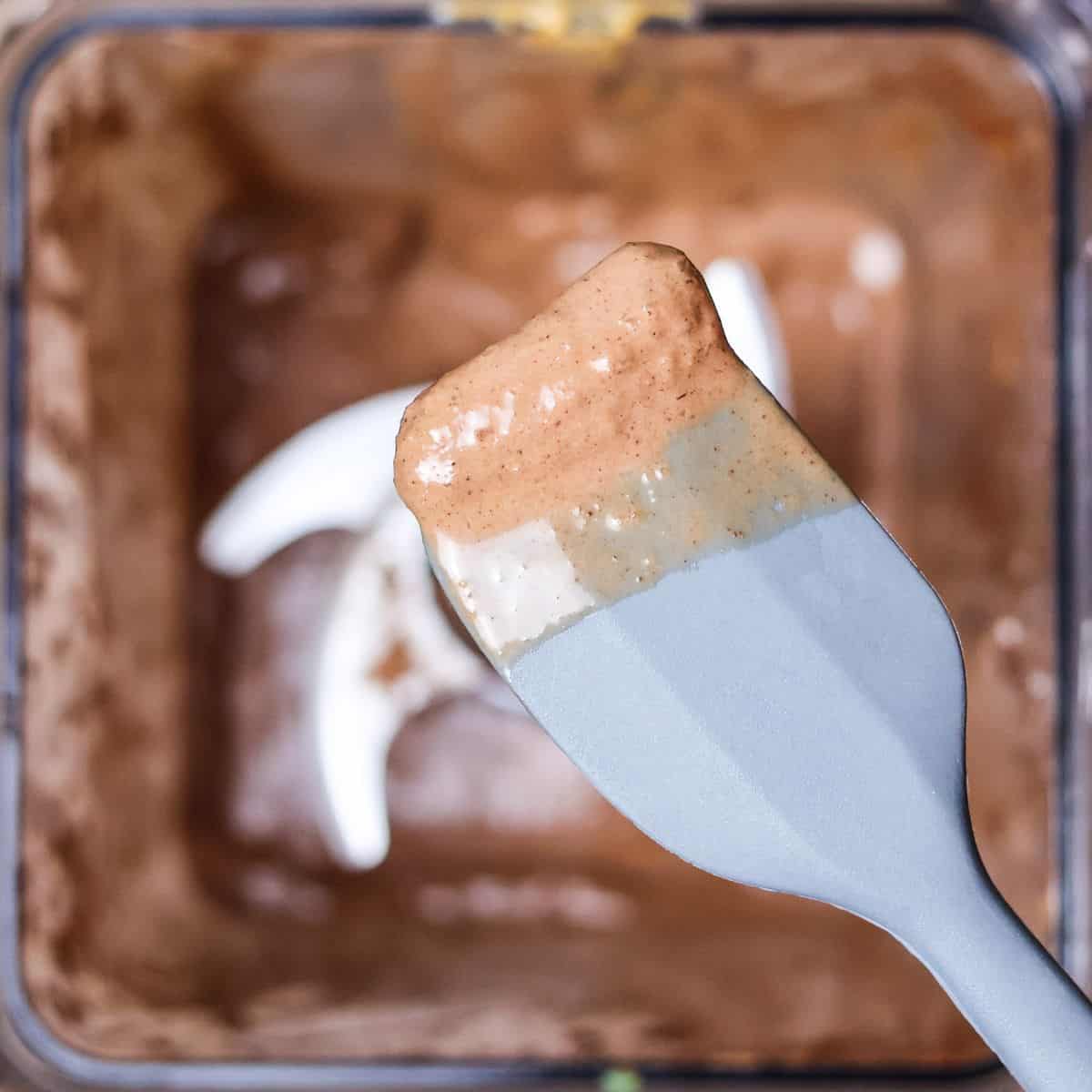 a small spatula with a scoop of chocolate peanut butter smoothie on it above the blender, indicating scooping a little out for a taste test.