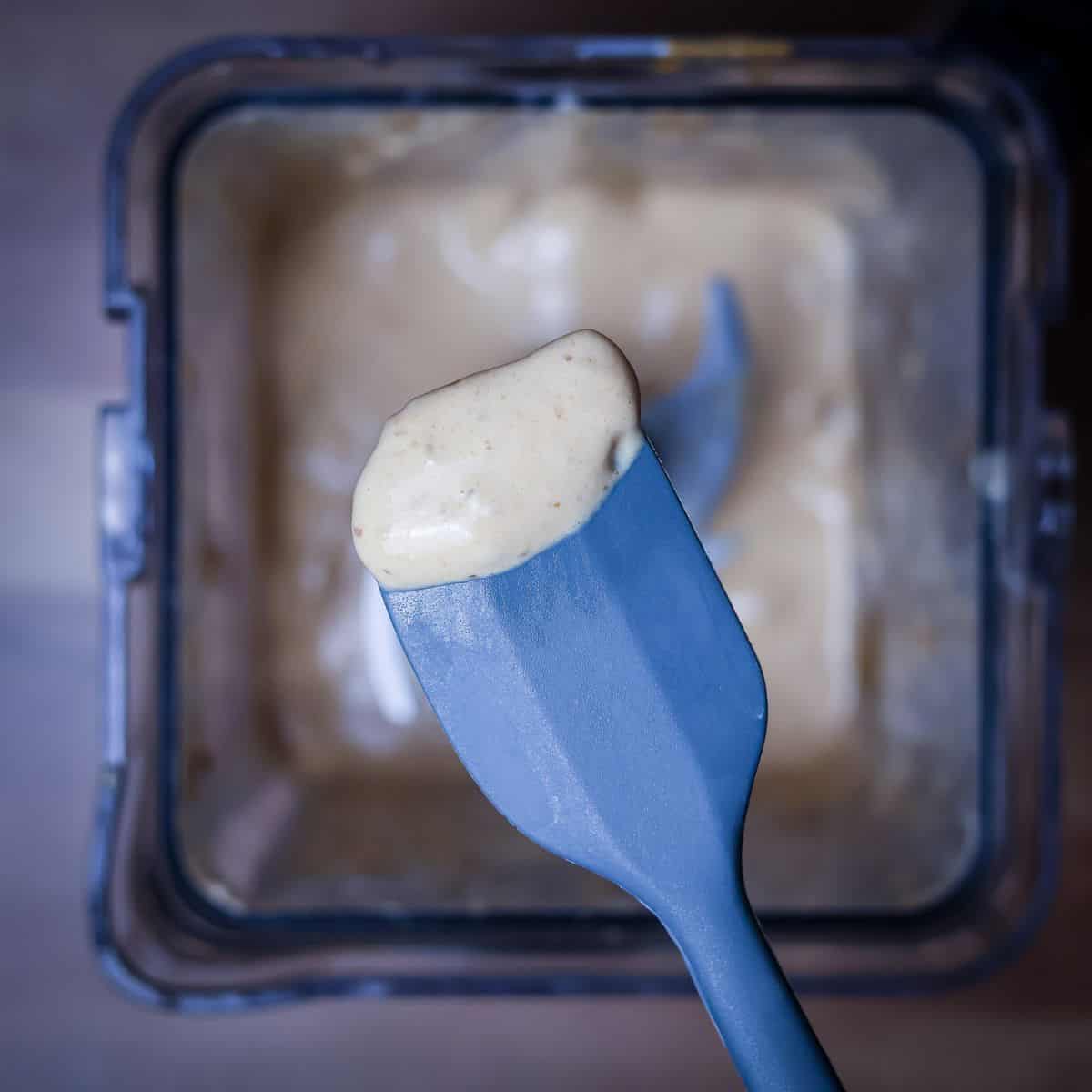 Close-up of a spatula with a thick, creamy health nut smoothie mixture to show the texture, with the blender in the background.