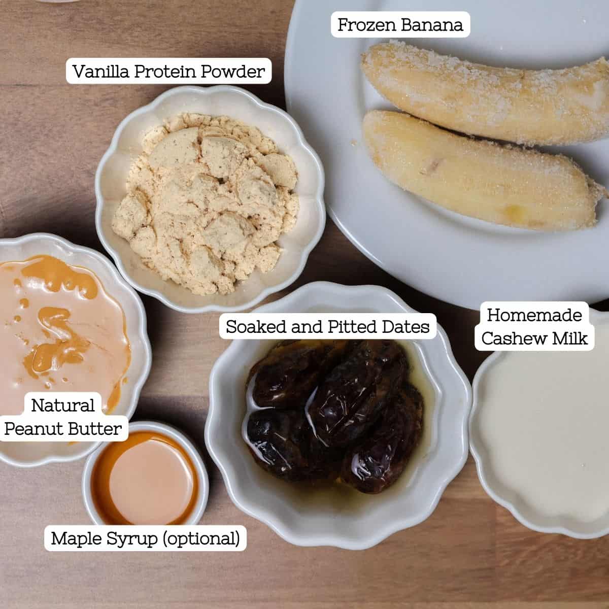 Ingredients for the health nut smoothie displayed in small bowls: natural peanut butter, vanilla protein powder, soaked and pitted dates, frozen banana, homemade cashew milk, and maple syrup.