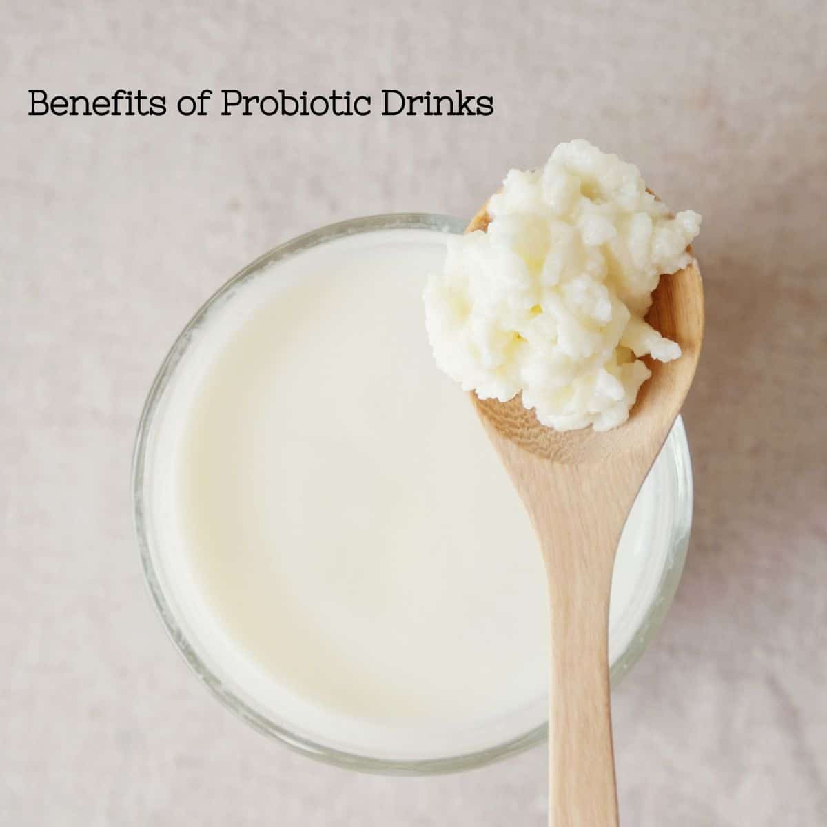 A photo of kefir and a wooden spoon full of kefir starter with the words that say "Benefits of probiotic drinks".