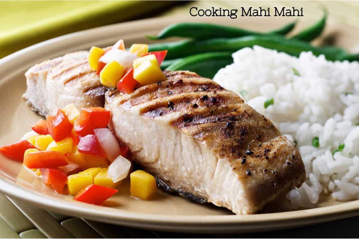 A perfectly cooked pair of mahi mahi fillets with yellow and red salsa on top and a bed of rice behind it on a plate/