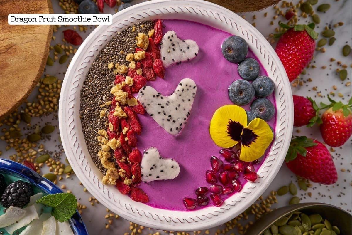 A beautifully decorates pink dragon fruit smoothie bowl covered in superfood toppings like nuts, seeds, and fruit.