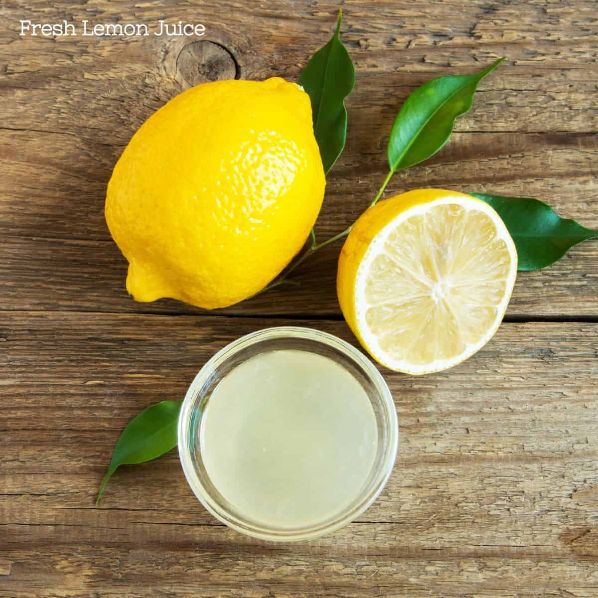 One whole lemon with green leaves and one cut lemon next to a glass of lemon juice.